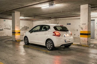 Peugeot 208 blanche entrant dans un parking souterrain avec plafond bas et piliers étroits